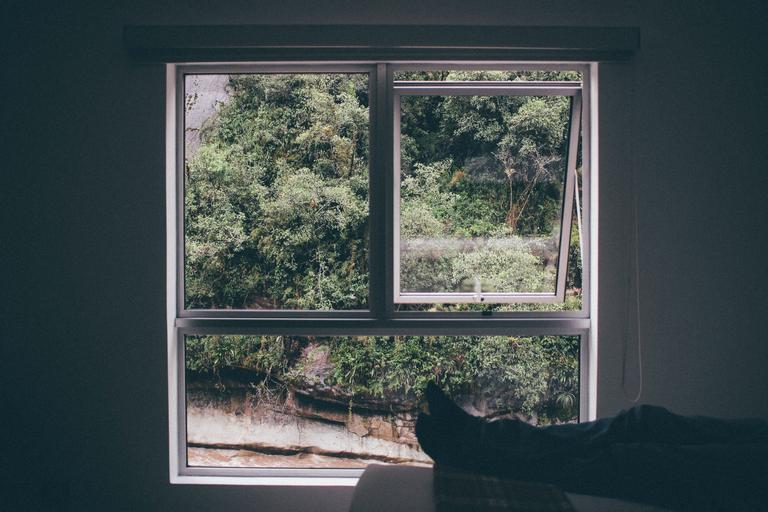 Hliníkové veľké okno na sivej stene, pri ktorom sedí človek s vyloženými nohami
